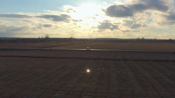 Aerial View Car Rides on The Road in The Field at Sunset alt