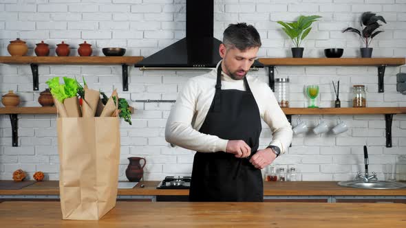 Man in sweater comes to home kitchen puts on apron preparing cook healthy food alt