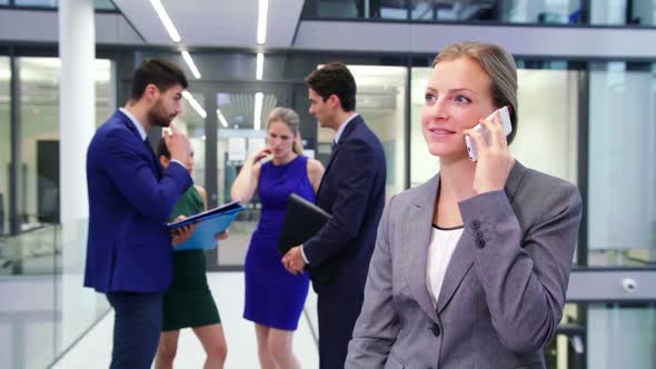 Businesswoman talking on mobile phone while businesspeople discussing in background alt