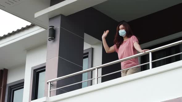 quarantine woman wearing a face mask and greeting neighbors from balcony of the home