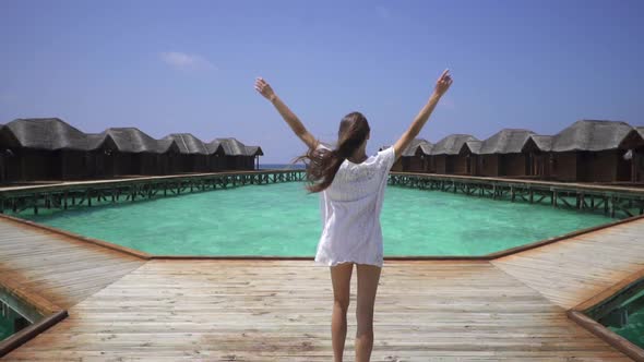 Beautiful sexy lady in white dress resting in Maldives. Walking on pier near water bungalows. alt