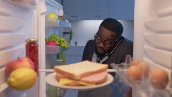 Busy businessman talking on phone and taking plate with sandwich