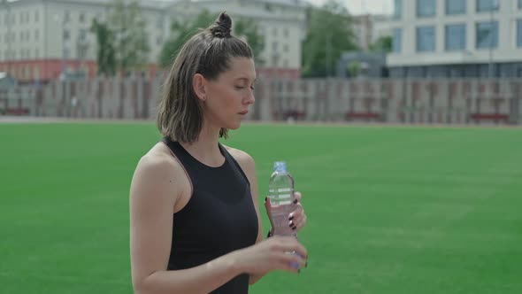 Young Athletic Woman Drinking Water From Bottle at Stadium After Training. alt
