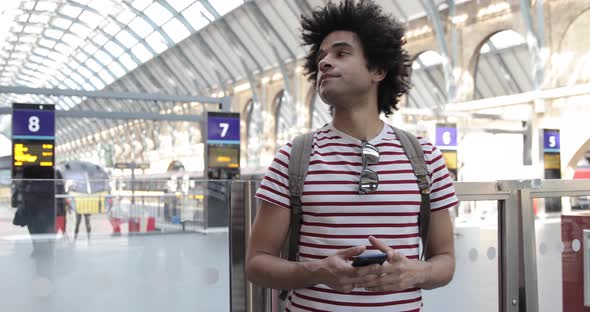 Man at train station checking timetables on mobile phone alt