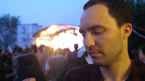 Man using a phone texting a message at concert. alt