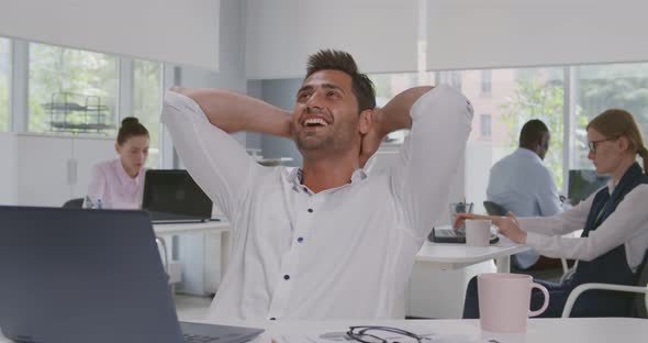 Indian Young Businessman Relaxing on Chair Behind Desk at Office alt
