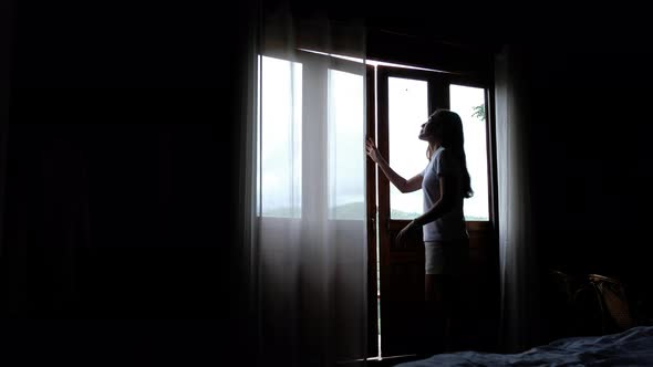 A woman opening curtains and wooden doors to see a beautiful greenery mountains view outside