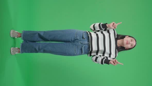Full Body Of An Asian Woman Pointing Up While Standing In Front Of Green Screen Background alt