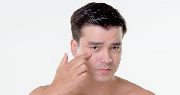 Beauty shot of young Hispanic man checking wrinkles on his face in white isolated background