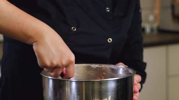 The Cook is Mixing Brown Creme in Steel Bowl for Making Dessert Closeup