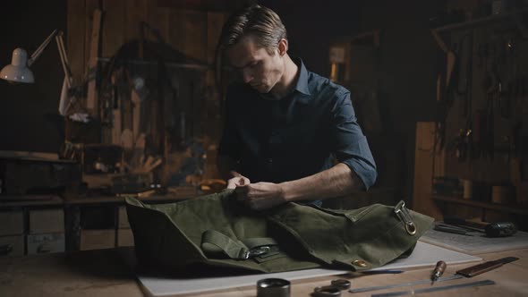 Young Man Tailor Unpicking Canvas Product at Workshop Preparing Fabric for Reuse in Evening Tracking alt