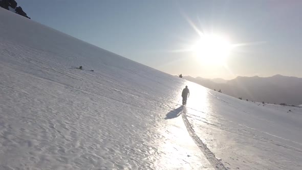 Dolly in following a man skiing alone across snow covered Piltriquitron Hill at sunset, El Bolsón, P alt