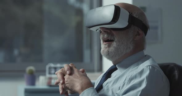 Excited mature businessman wearing a VR headset and experiencing virtual reality in his office