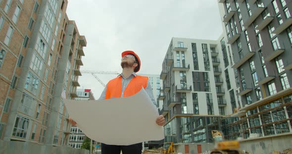 Close-up Portrait of Engineer with Blueprint on Background of Building Under Construction. Young alt