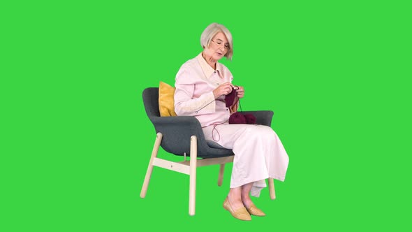 Mature Grandmother Sitting and Knitting and Telling a Story To Camera on a Green Screen Chroma Key alt