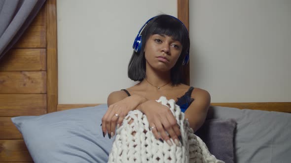 Melancholic Woman in Headphones Sitting on Bed alt