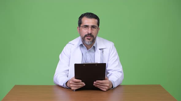 Handsome Persian Bearded Man Doctor Giving Consultation While Holding Clipboard