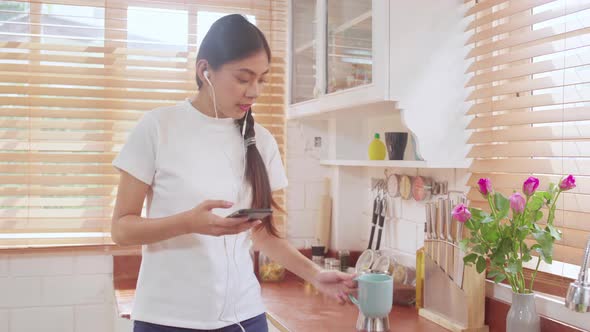 Young Asian teenager woman drinking warm coffee using smartphone listening music. alt