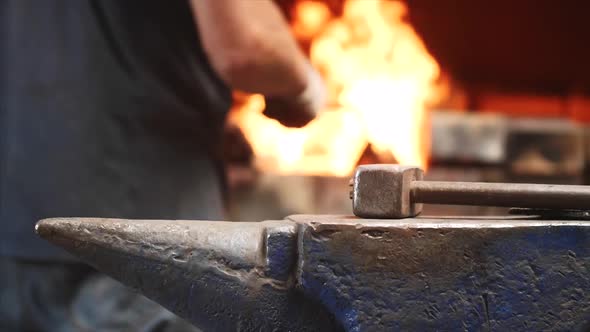 Hammer on Anvil and Hands of Worker on Background Put Wood in Furnace with Fire