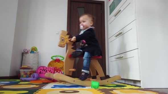 Happy baby girl playing on wooden rocking horse. Childhood, game at home concept alt