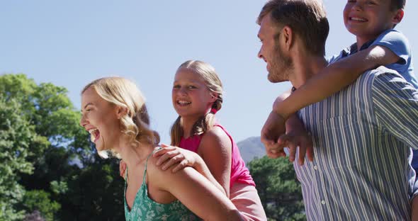 Caucasian father and mother giving piggy back rides to their kids in the garden alt