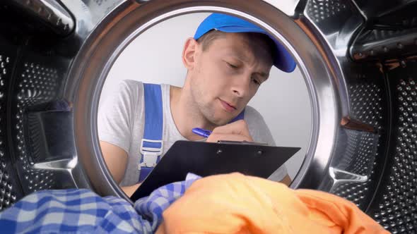 Washing machine repairman looks at drum and writes down list of works. alt