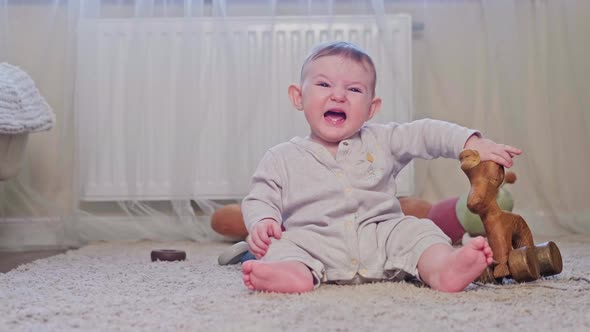 A small child is crying sitting on the carpet in the nursery. Toddler baby boy is naughty