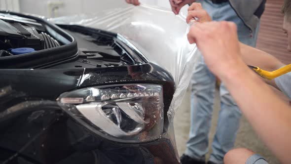Detailing Service Team Applying Protective Film During Work in Garage alt
