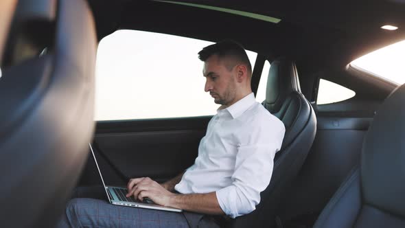 Businessman Working on Laptop Computer in the Back Seat of a Car alt