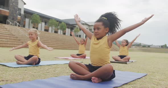 Video of focused diverse girls practicing yoga on mats in front of school alt