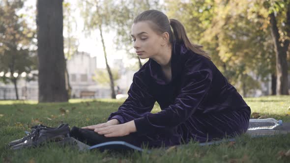 Positive Slim Beautiful Young Sportswoman Touching Toes Stretching on Exercise Mat Outdoors alt