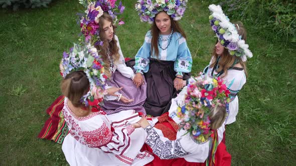 High Angle View of Beautiful Ukrainian Women in National Clothes Holding Hands Sitting on Green alt