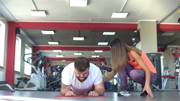 A Caucasian Man with a Beard Performs an Exercise in the Gym Plank, Next Beautiful Girl Coach alt