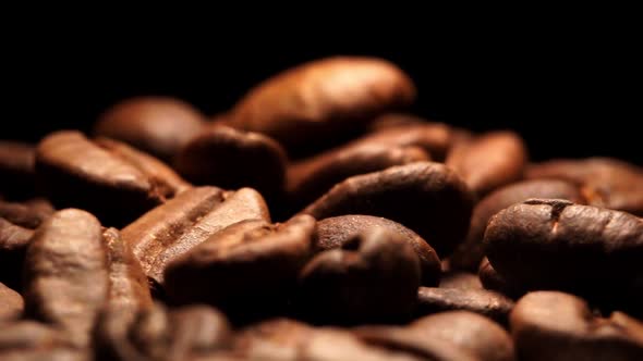 Close up view of fresh roasted Arabica coffee beans on black background drops from above