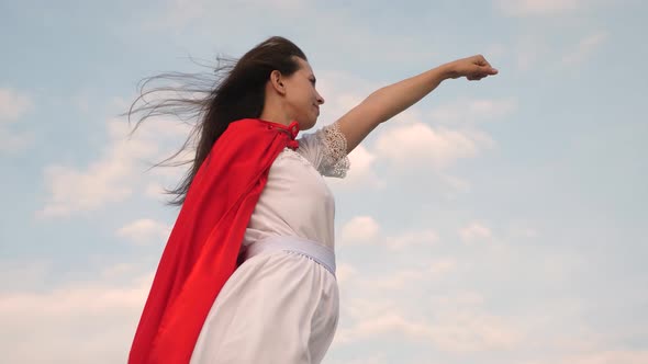 Beautiful Superhero Girl Standing on a Field in a Red Cloak, Cloak Fluttering in the Wind. Girl alt