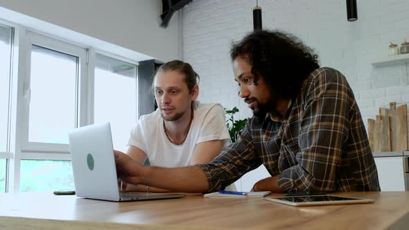 Two Young Freelance Guys Work Remotely At Home on an Online Project, Using a Laptop alt