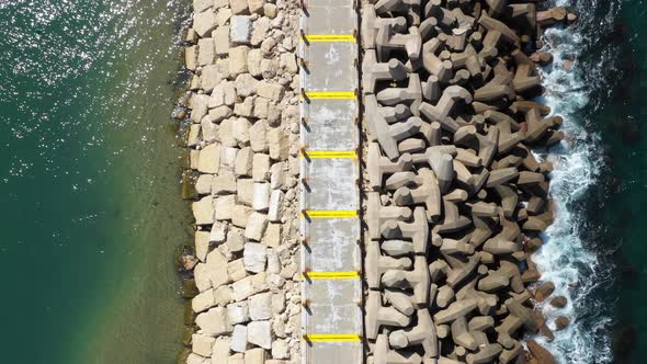 Small blue waves from the clear Mediterranean sea splash on the man-made pier with large unusually s alt