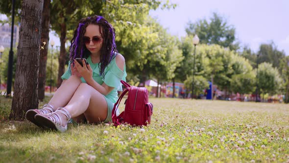 A young woman is resting in the shade of a tree in the park. alt
