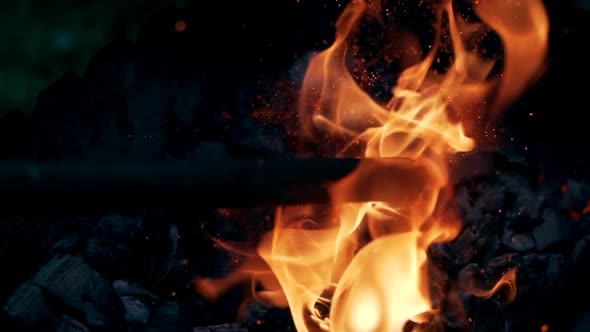 Wooden stick breaks smoldered logs in fire. Bright sparks moving on dark background  alt