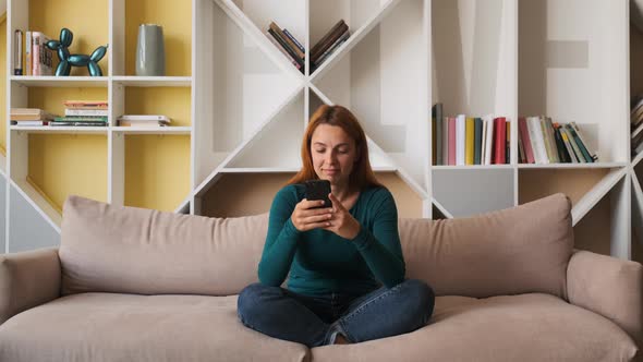 Beautiful Young Woman Holding Smartphone in the Living Room alt
