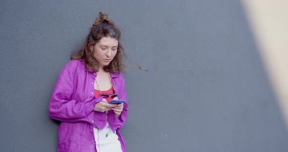 the girl leans against the wall and holds the phone in her hands alt
