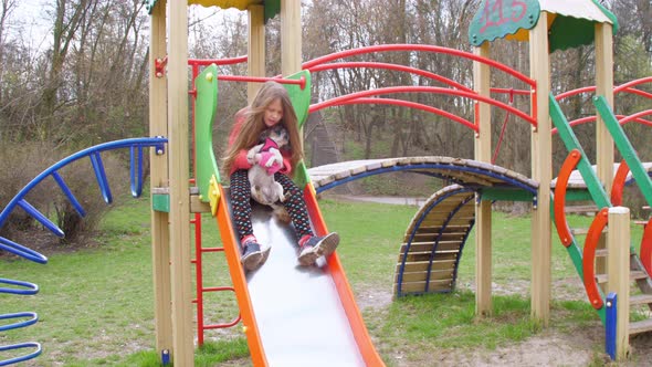 Junior Schoolgirl Blonde Sits on Attraction and Holds Dog alt