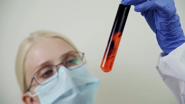 A Female Doctor Examines a Glass Flask Filled with Bluered Liquid