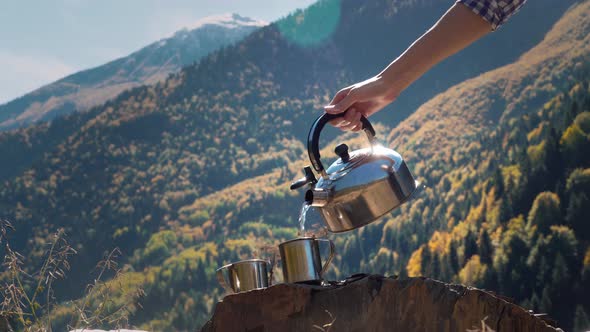 20    female traveler pours hot water from kettle into metal mug in close-up, alt