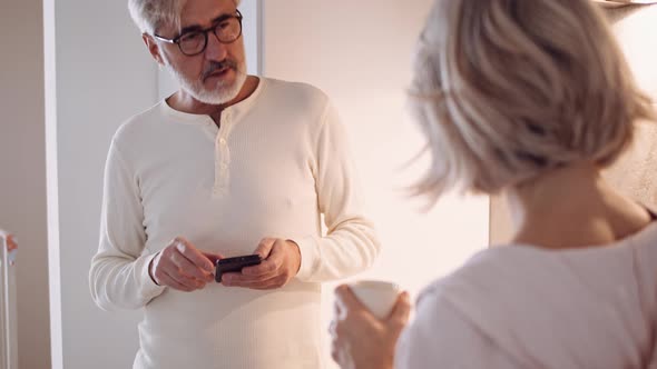 Slow motion shot of mature man using smartphone in the kitchen alt