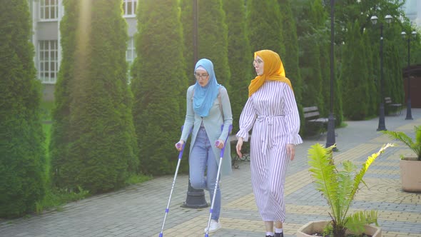 Muslim Woman with a Broken Leg on Crutches Communicates with Another Muslim Woman in a Traditional alt