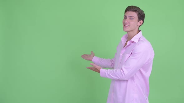 Happy Young Handsome Businessman Presenting Something To the Back alt