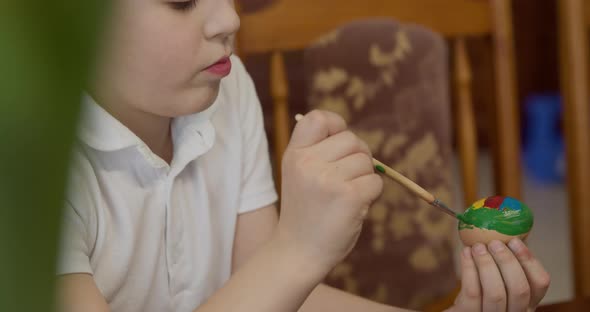 a Boy Paints an Easter Egg with a Brush alt