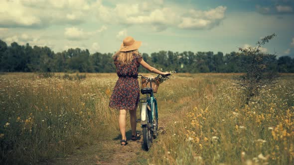 Tourist Girl Relaxing On Countryside Wildflower Field.Woman Cyclist Walking With Bike. alt