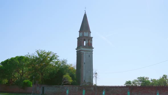 Church Bell Tower with Brick Fence Stands Among Trees alt